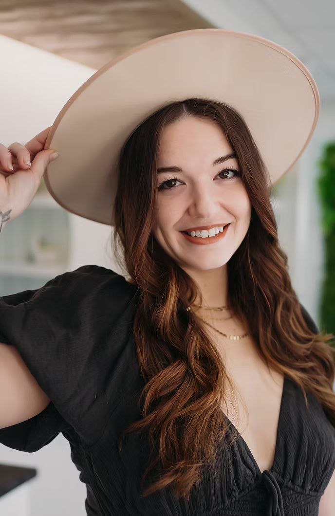 A woman wearing a hat and a black dress is smiling.