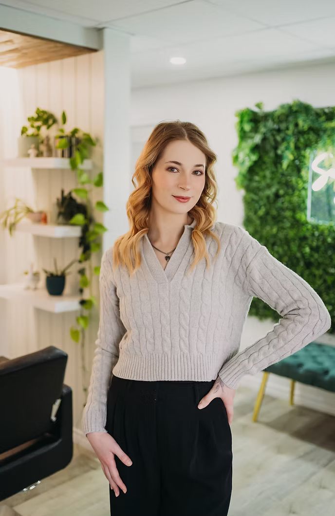 A woman in a sweater and black pants is standing in a room with her hands on her hips.