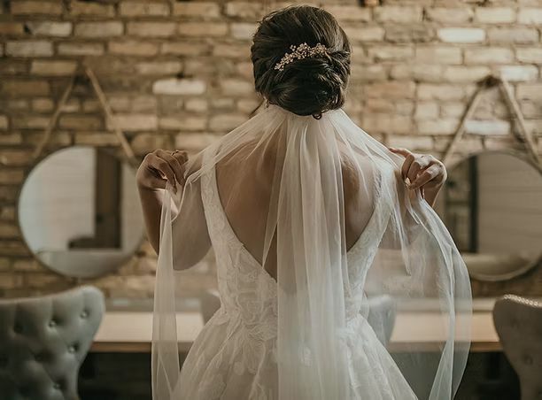 A bride in a wedding dress and veil is standing in front of a brick wall.