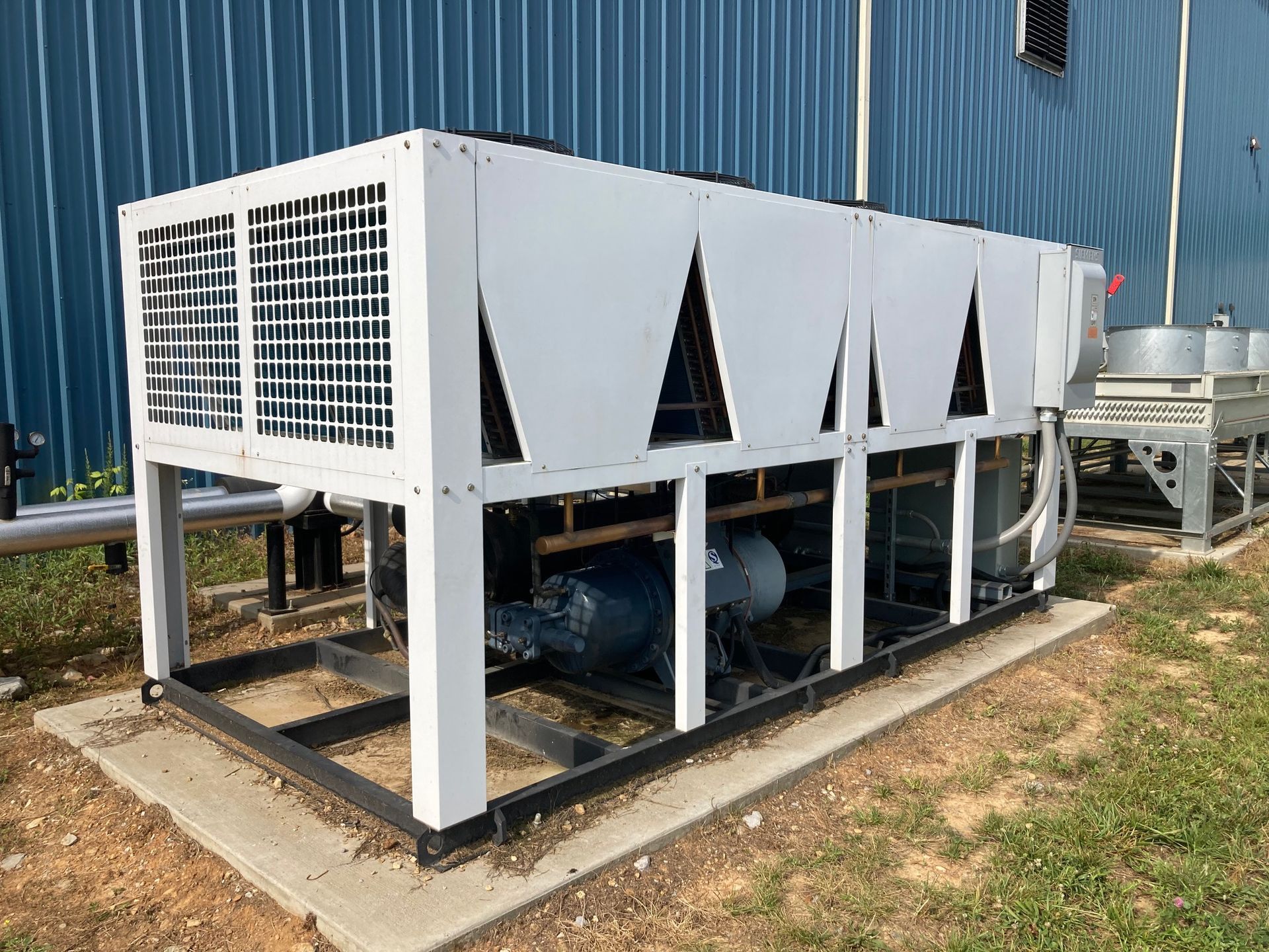 A large white machine is sitting in front of a blue building.