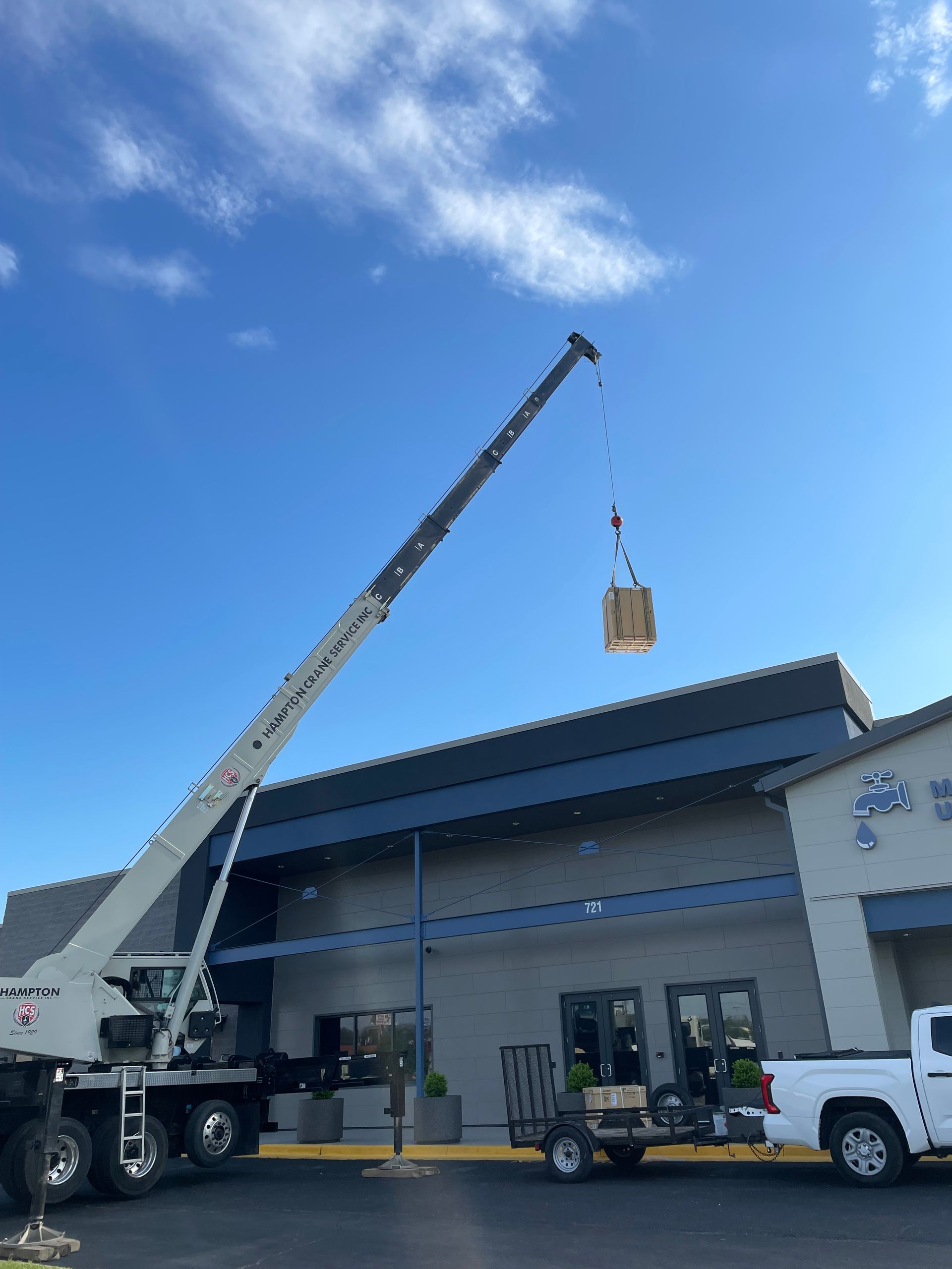 A crane is lifting a box into the air in front of a building.