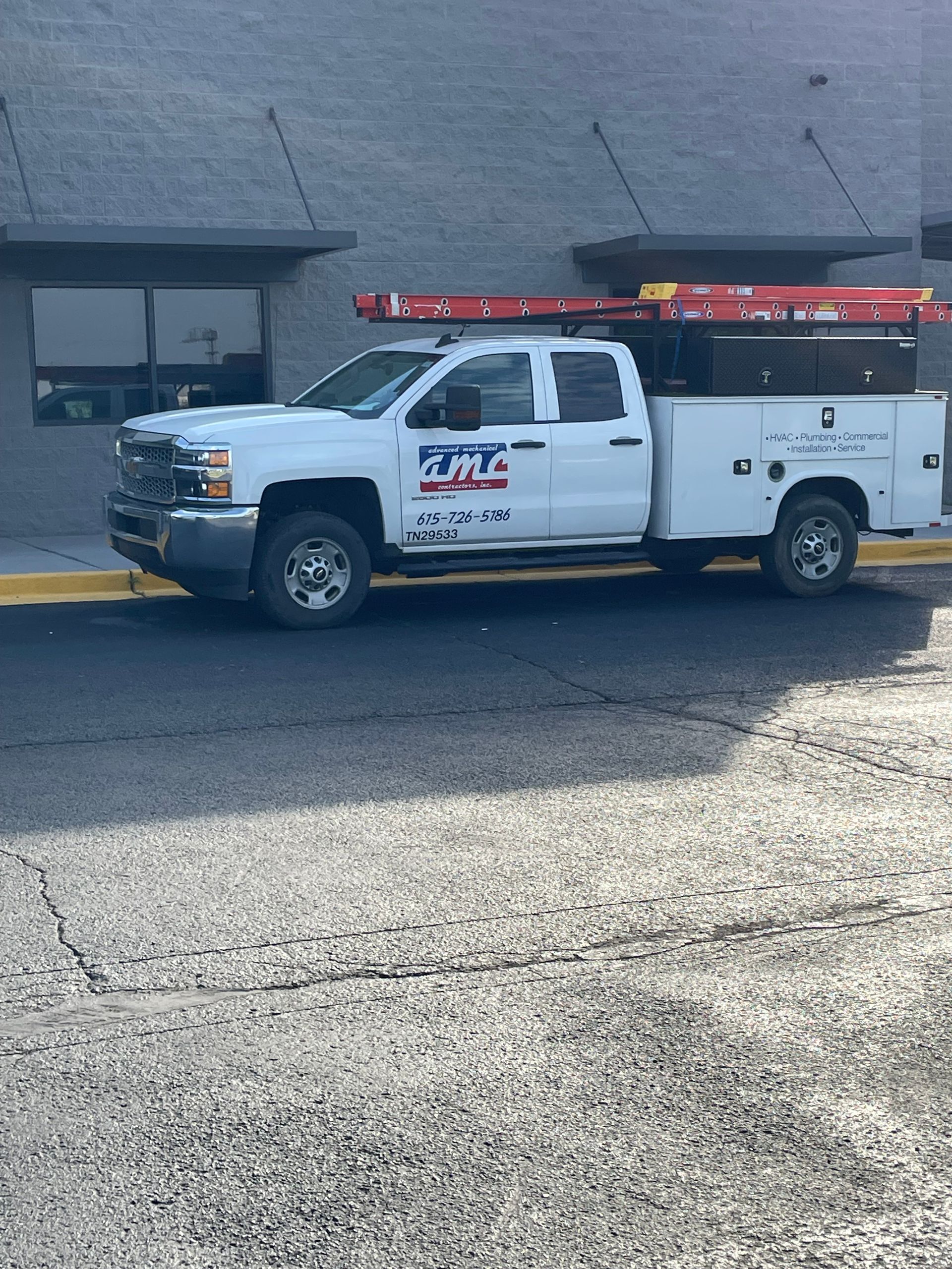 A white truck with a ladder on top of it is parked in front of a building.