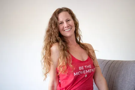 Woman with long curly hair smiles, wearing a red tank top that says 