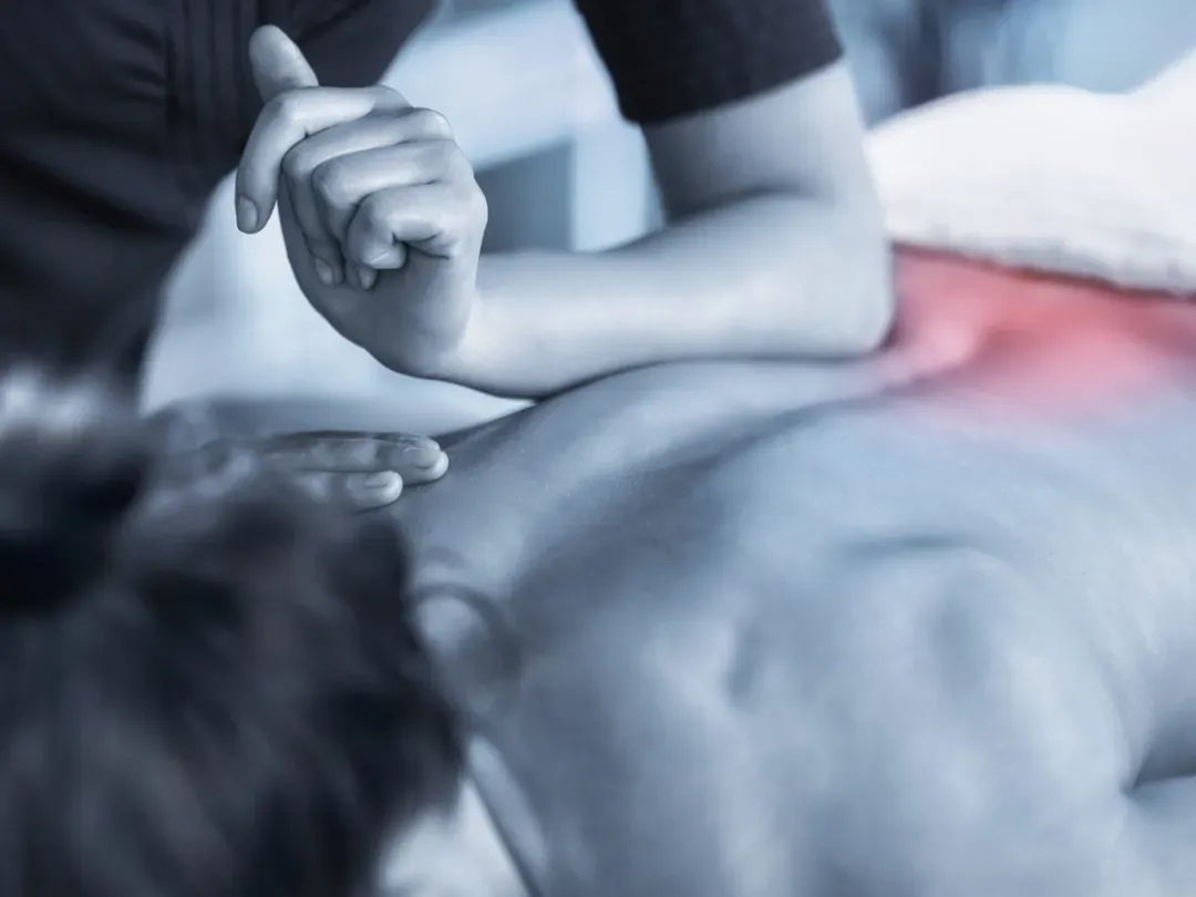 Person receiving a massage. Masseuse's elbow on back, targeting a red, painful area. Blue-toned.