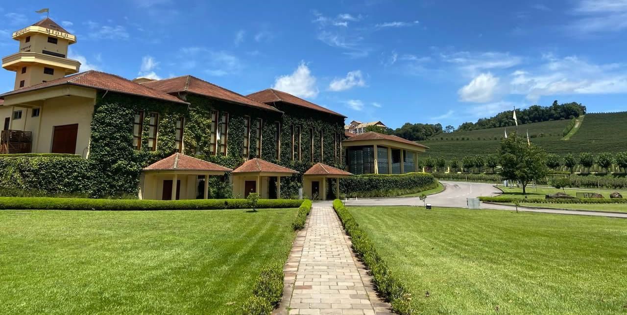 Um grande edifício com telhado de telhas vermelhas é cercado por um campo verdejante.- Pousada Santo Antônio