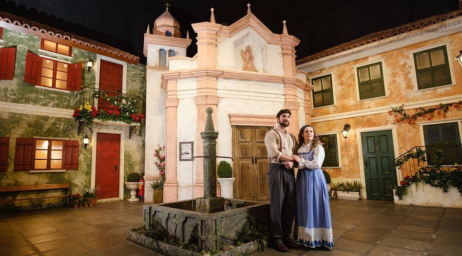 Um homem e uma mulher estão parados em frente a uma igreja.- Pousada Santo Antônio
