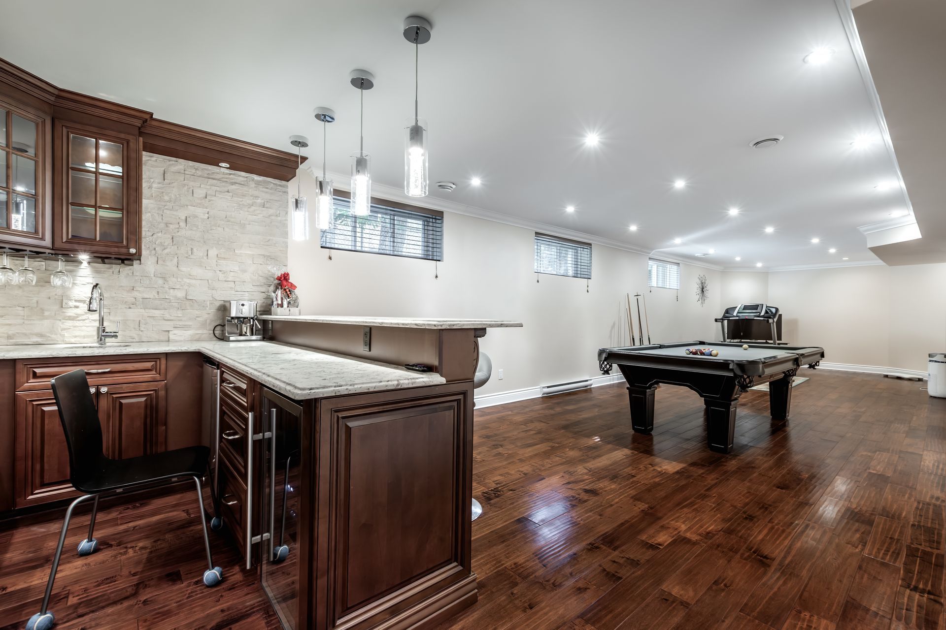 A basement recreation room with a bar, pool table, and wood flooring.