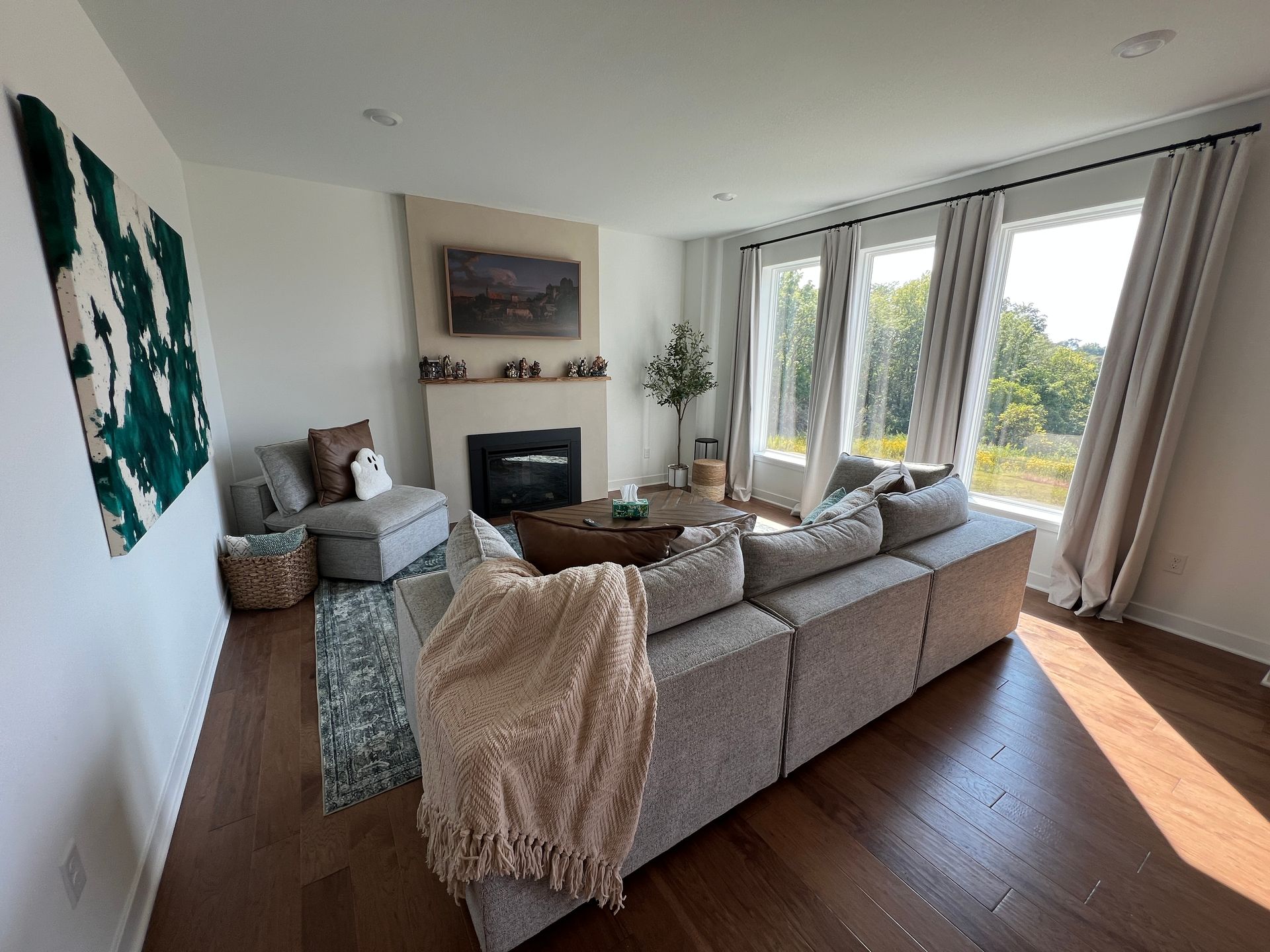 Cozy living room with large sectional, fireplace, windows, hardwood floor, and abstract art.
