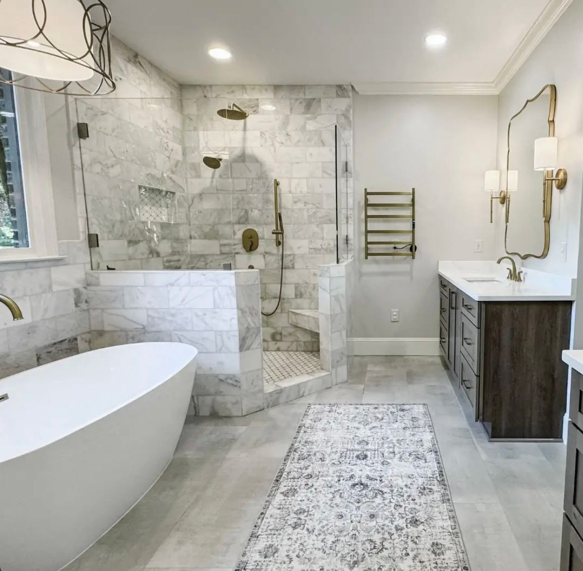 Luxurious modern bathroom: white soaking tub, marble shower with gold fixtures, gray vanity.