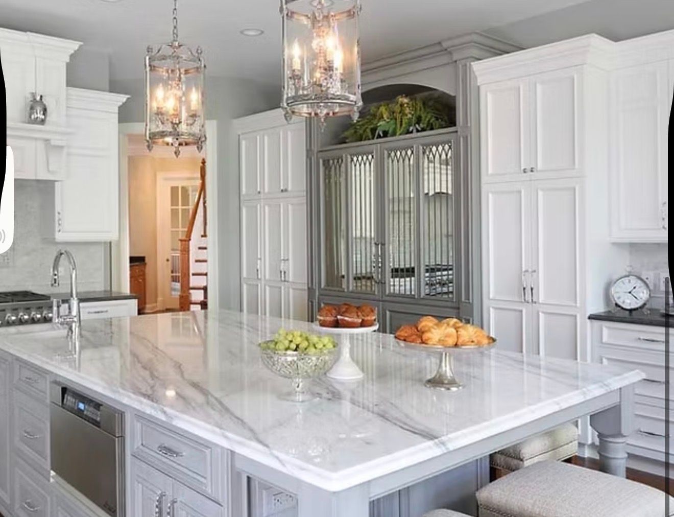 Elegant white kitchen with marble island, ornate lighting, and pastries.