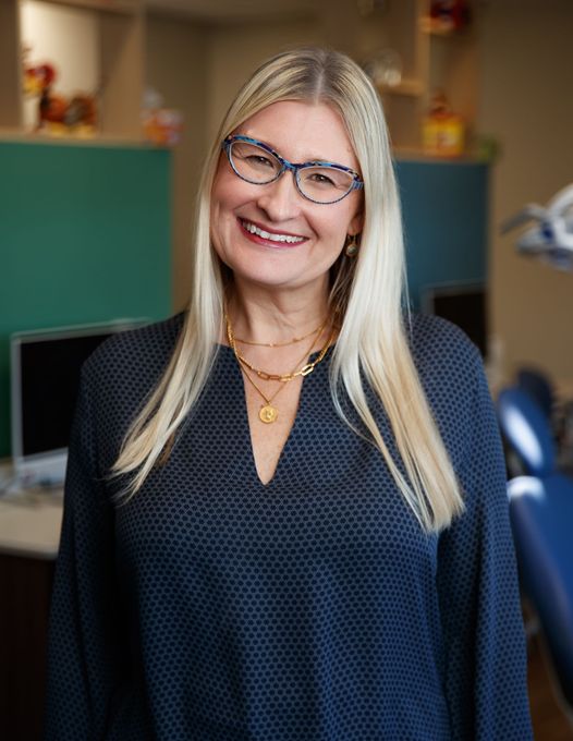 A photo of Dr. Jill Jenkins smiling at the camera. She has blond hair, brown eyes, and blue glasses.