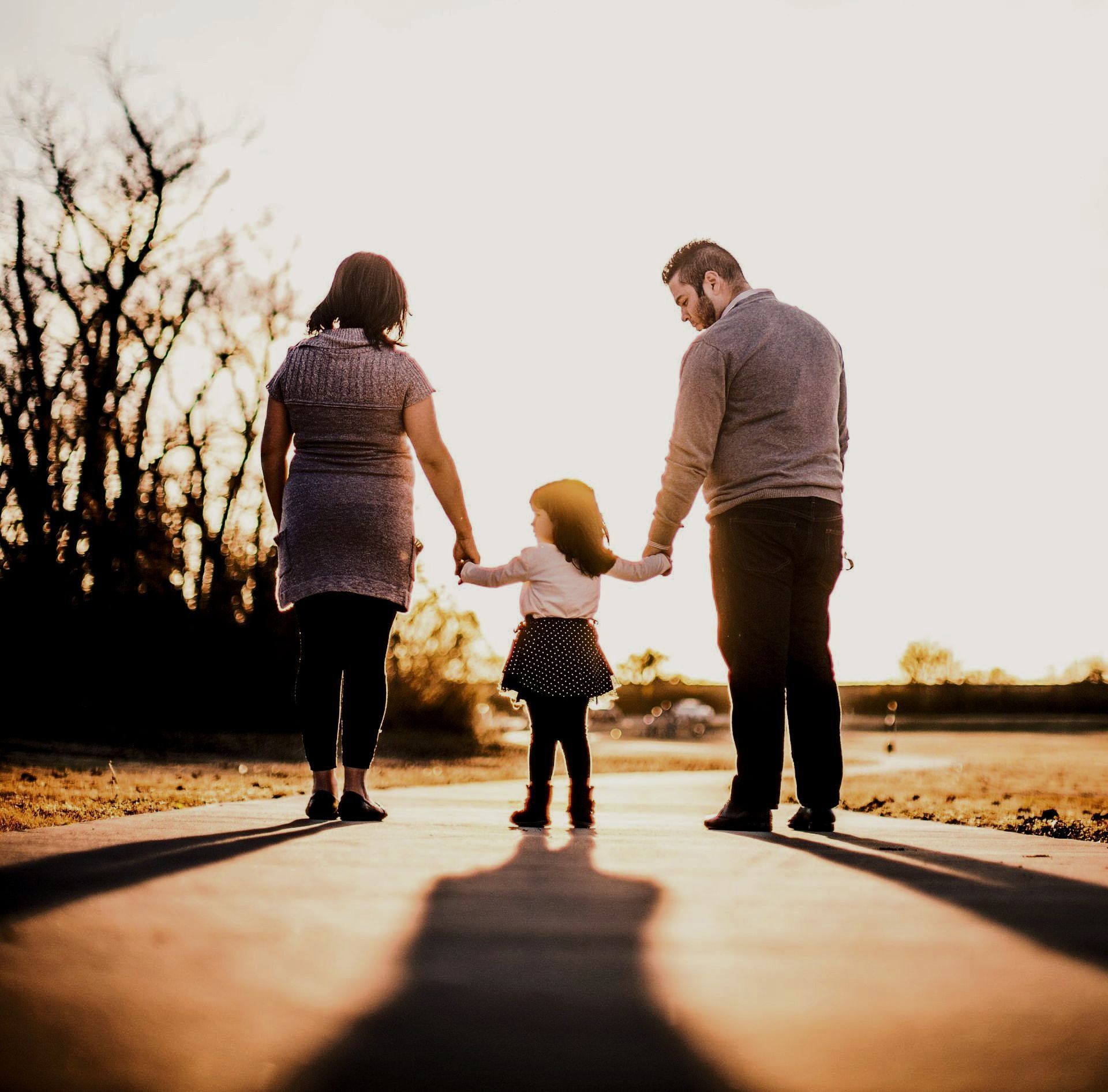 a family is walking down a sidewalk holding hands .