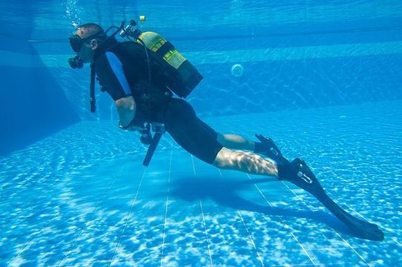 A scuba diver is swimming underwater in a pool.