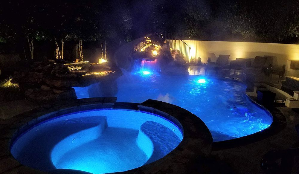 A large swimming pool is lit up at night with blue lights.