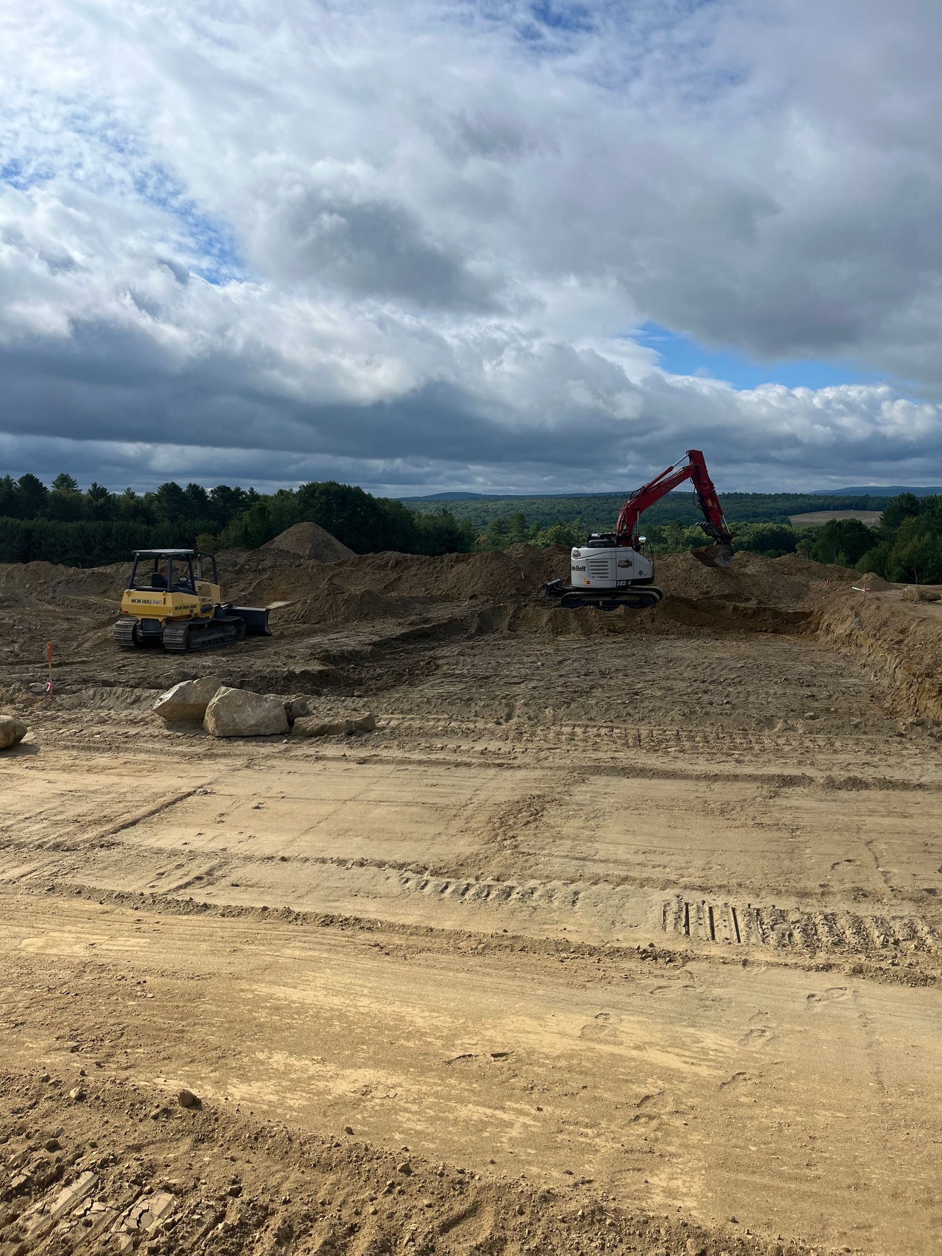 Construction site with a yellow bulldozer and a red excavator working on dirt, under a cloudy sky.