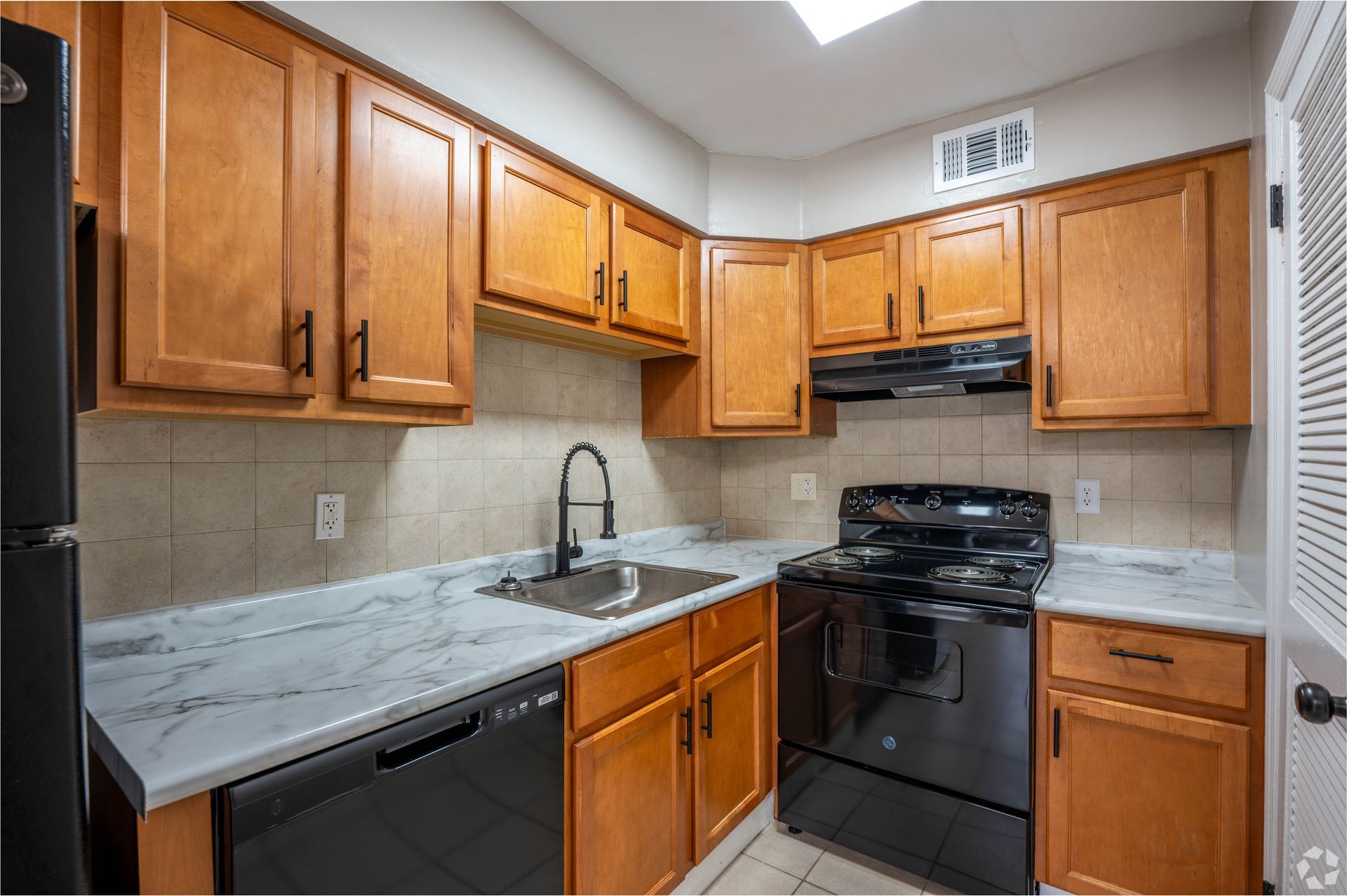Kitchen with wood cabinets, black appliances, and light countertops.