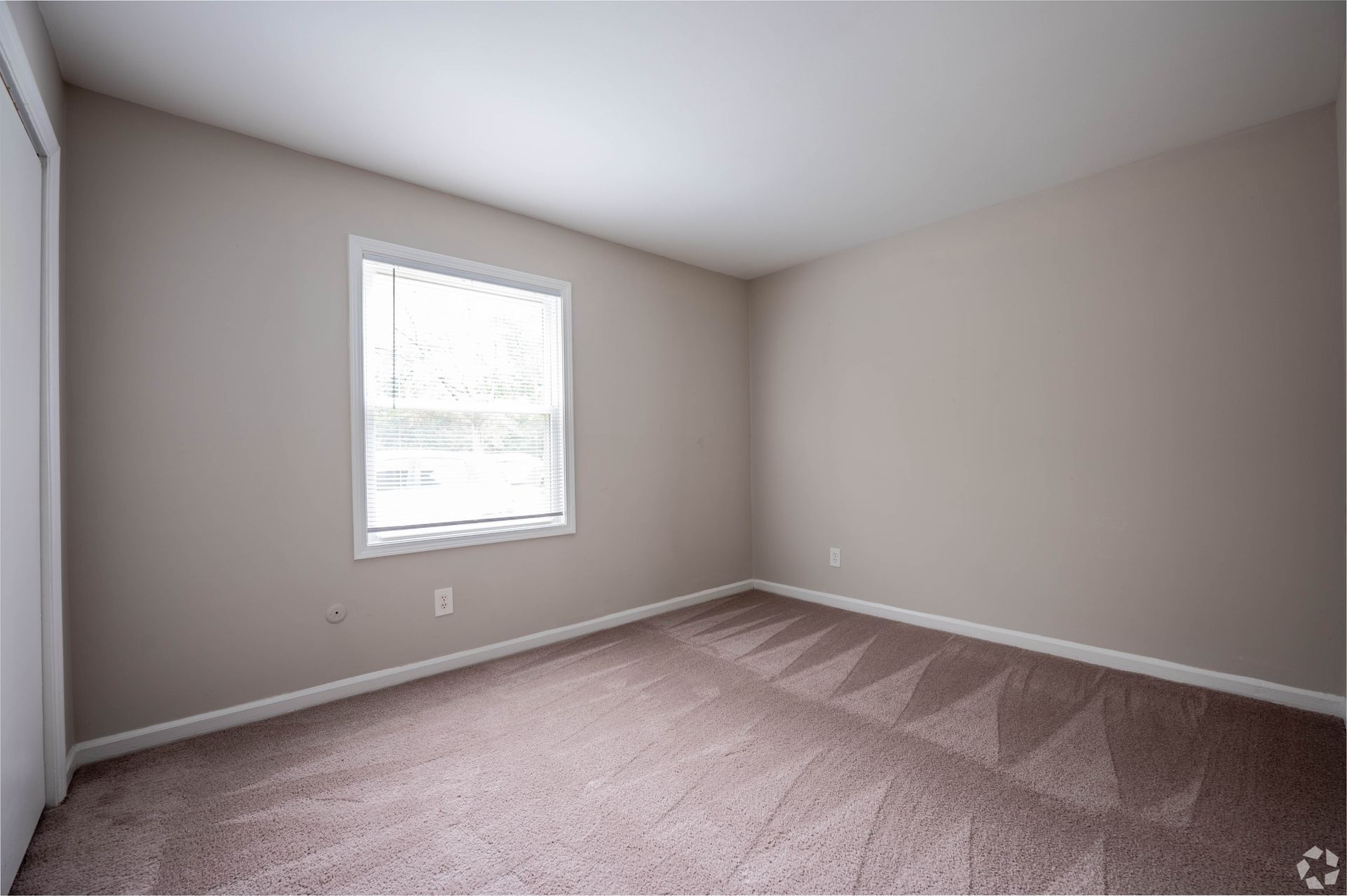 Empty bedroom with neutral walls, window, and patterned carpet.