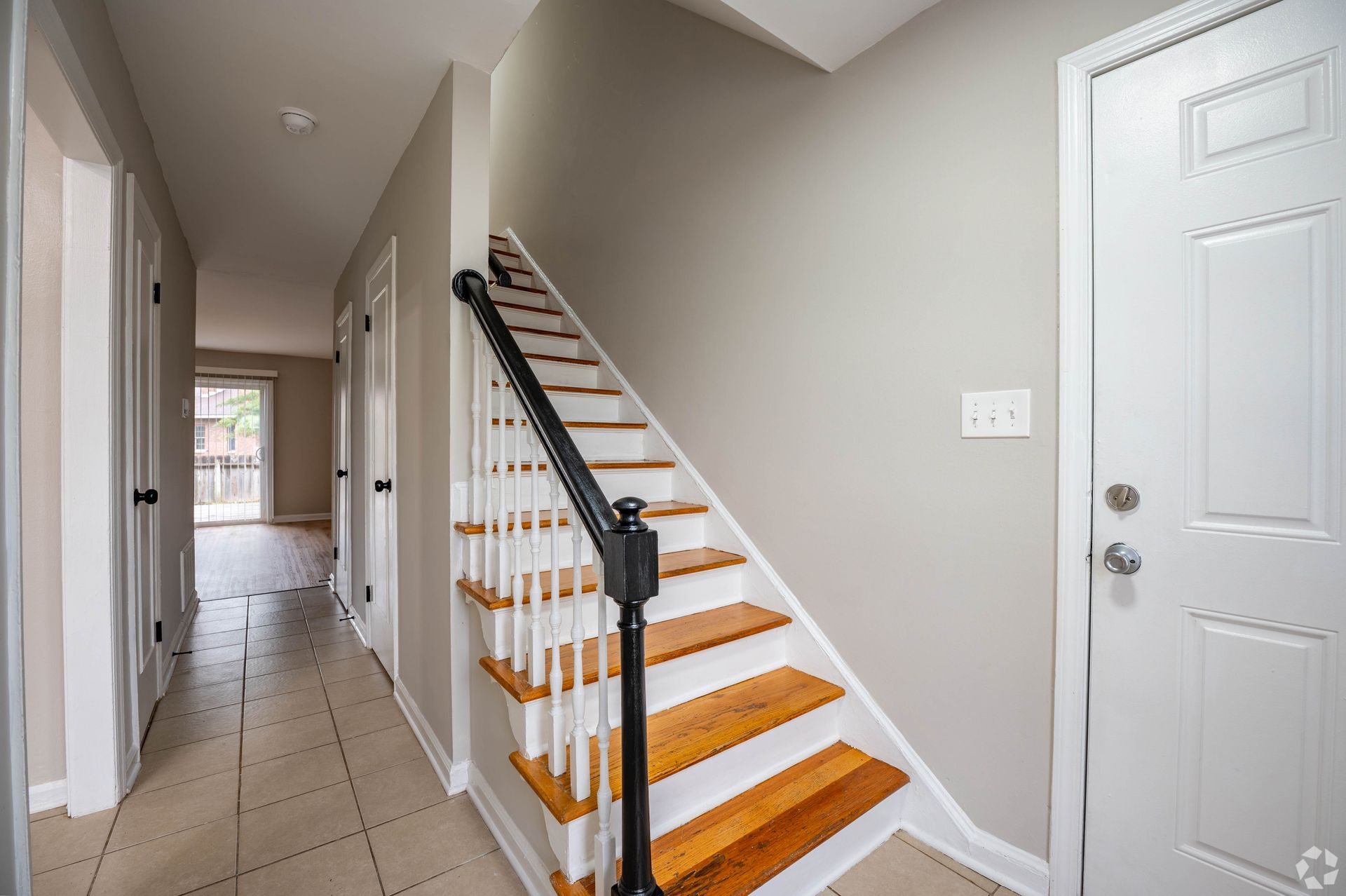 Hallway with stairs, a white door, and beige tile flooring.
