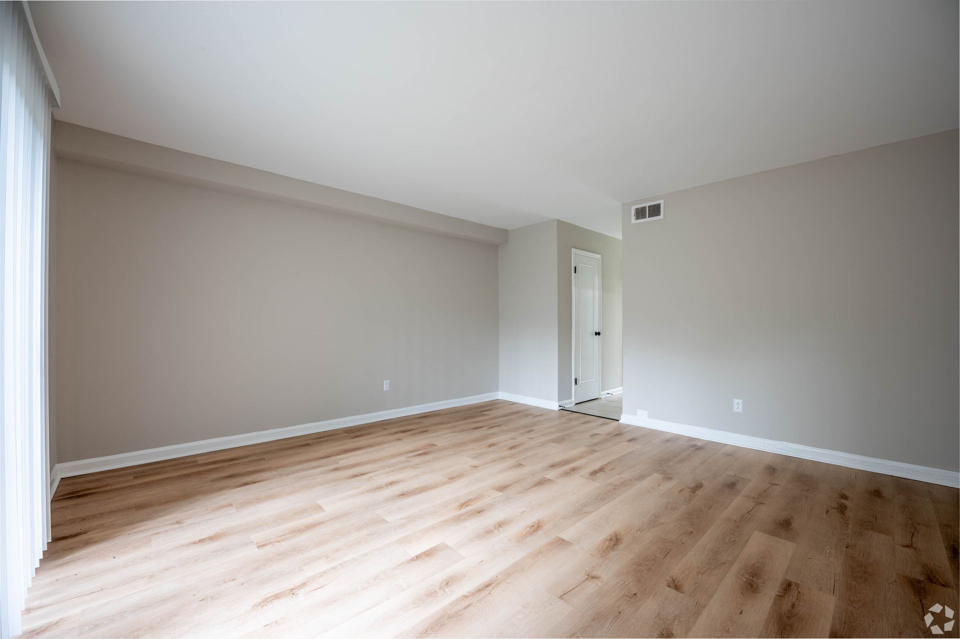 Empty room with beige walls, wood-look floor, white trim and door.