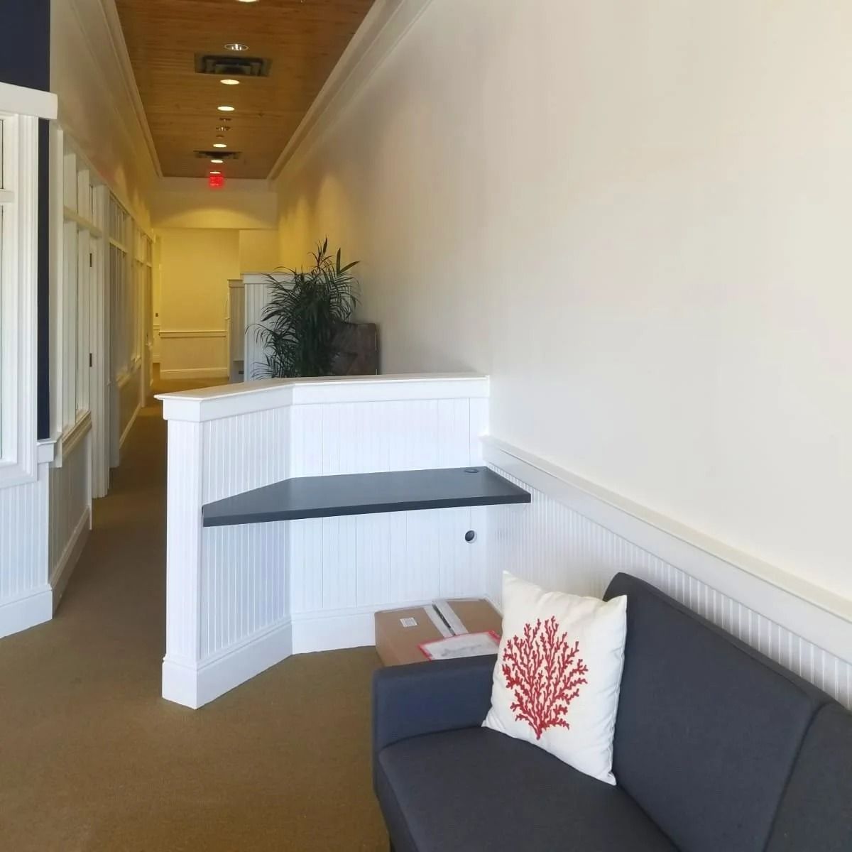 Hallway with white walls, a built-in desk, and a gray sofa with a coral pillow.