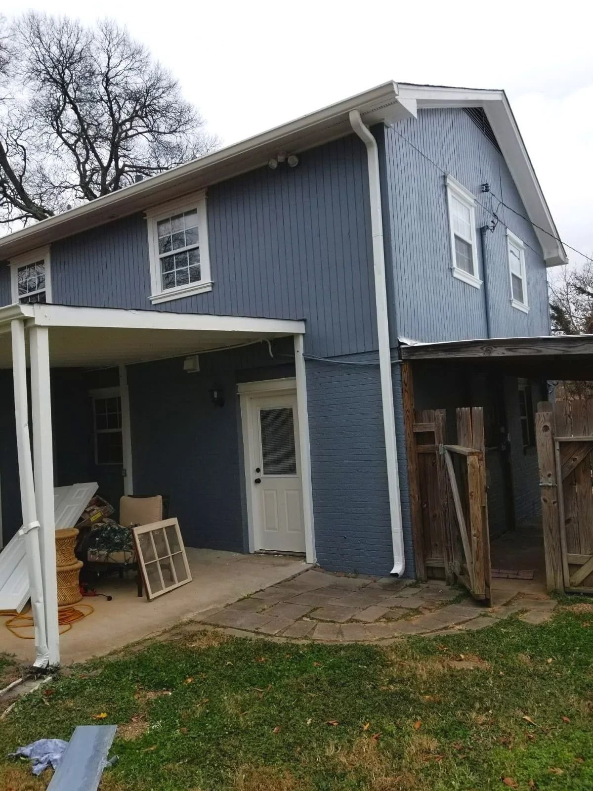 Blue-sided two-story house with white trim, door, and porch, backyard setting, overcast sky.