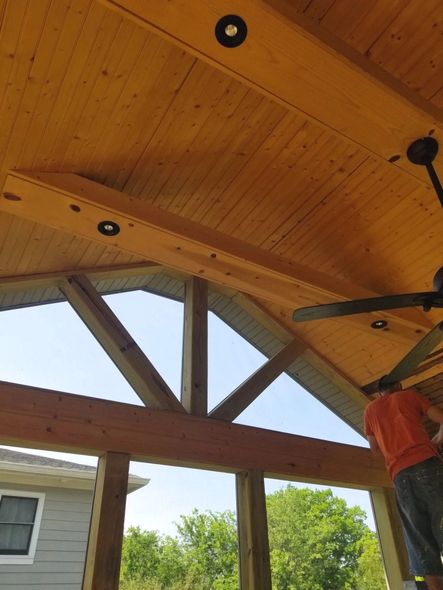 Wood-paneled porch ceiling with recessed lights and a fan; a person is working near the fan.