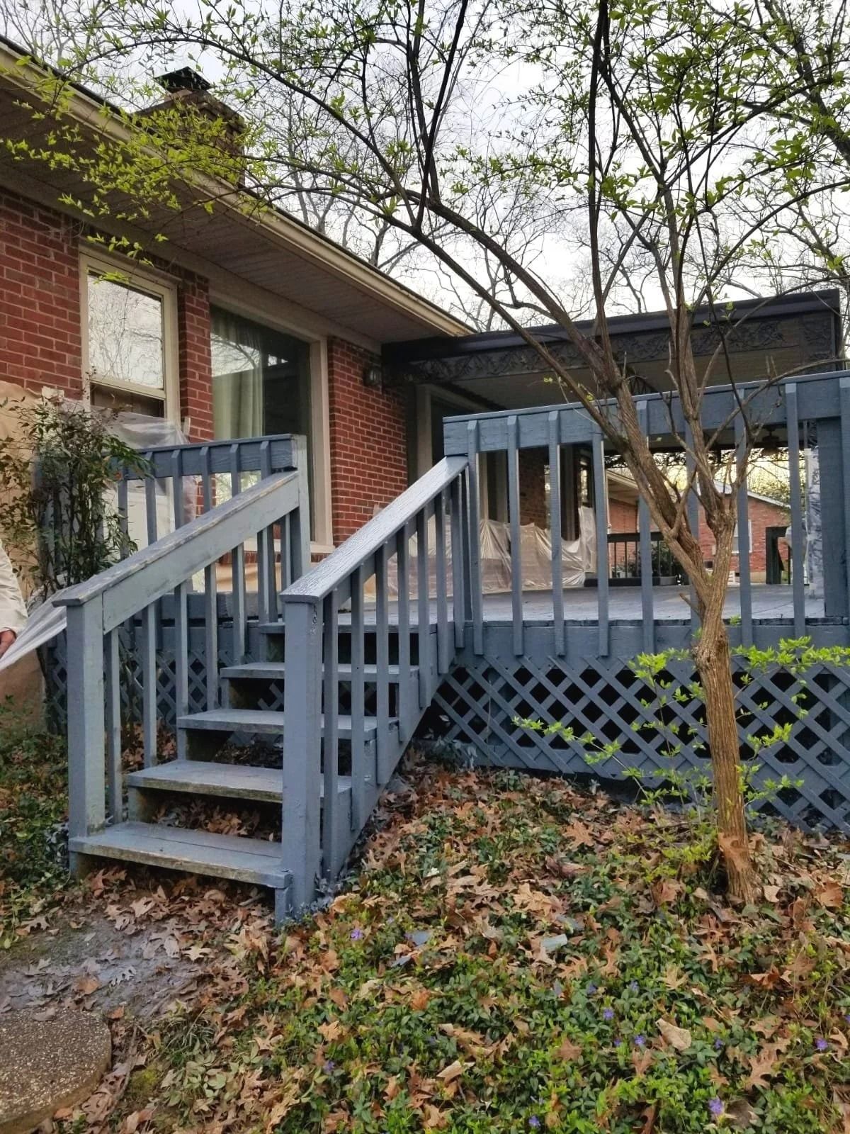 Wooden deck with stairs, painted grey, attached to a brick house.