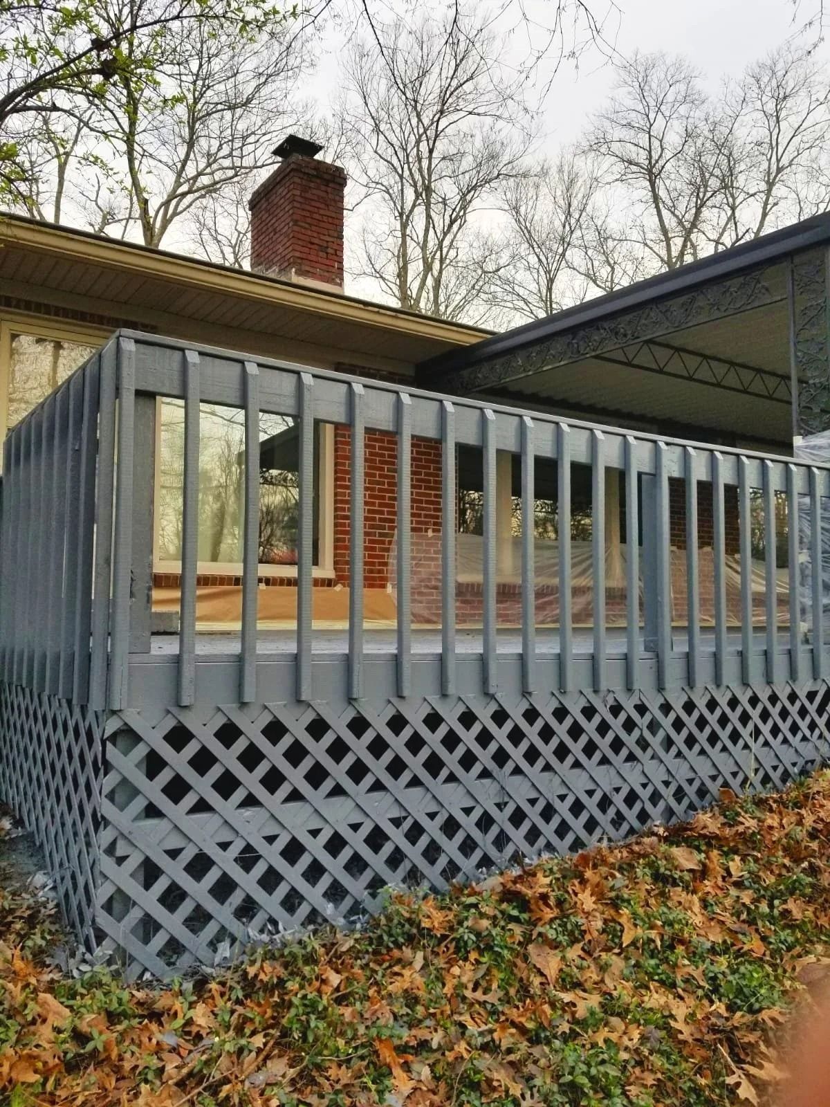 Gray painted deck with lattice, brick chimney, and bare trees.
