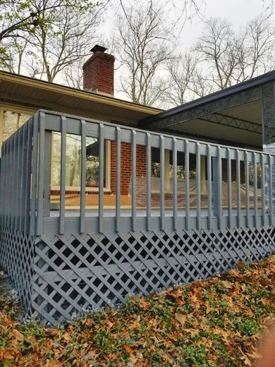 Gray painted deck with lattice skirting, against a house and under trees.
