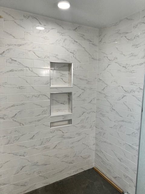 White marble-patterned tiled shower with three built-in niches. Dark concrete floor.