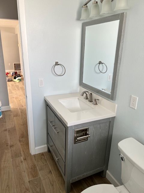 Bathroom with gray vanity, white countertop, mirror, and toilet. Light blue walls, wood-look floor.