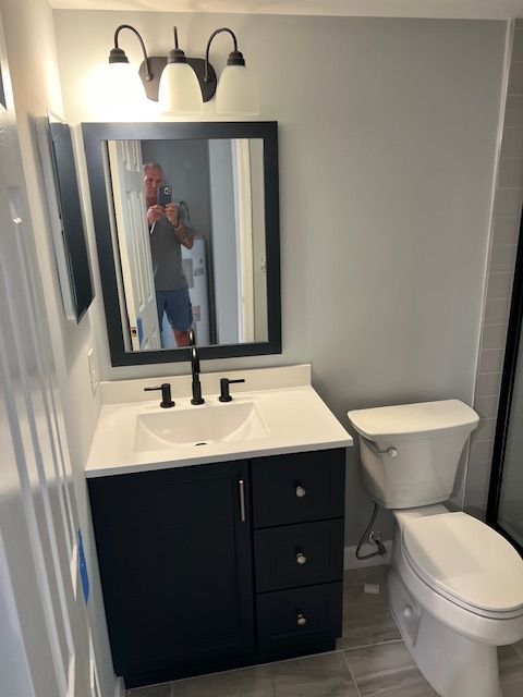 Bathroom with black vanity, white countertop, mirror, toilet, gray walls, and lights.