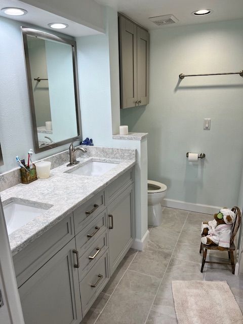 Bathroom with light gray cabinets, white sinks, gray countertops, and light blue walls.