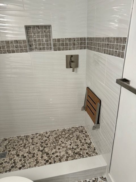 A modern shower with white and mosaic tiles, a wooden fold-down seat, and a built-in shower niche.
