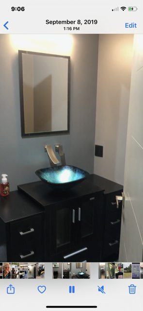Bathroom with black cabinet, blue glass sink, and a rectangular mirror. Grey walls.