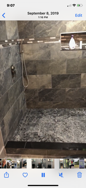 Bathroom shower with dark grey and brown tile and stone flooring, showerhead, and recessed shelf.