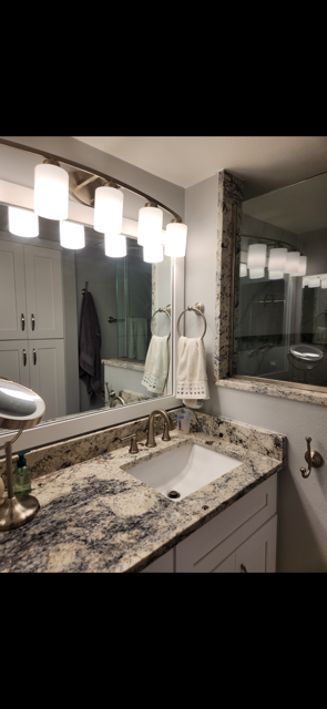 Bathroom with a granite countertop, white cabinets, and a large mirror with a light fixture above the sink.