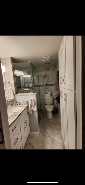 Bathroom with white cabinets, marble floors and walls, toilet and shower stall.
