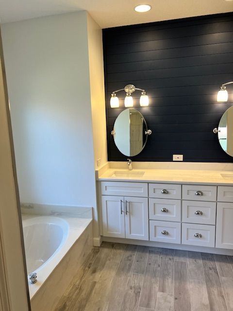Bathroom with blue shiplap accent wall, white vanity, oval mirrors, and gray wood-look floor.