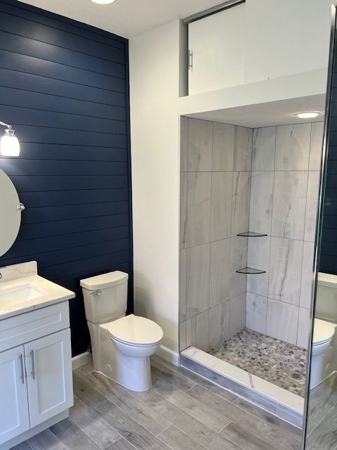 Bathroom with blue shiplap wall, white vanity, and tiled shower with pebble floor.