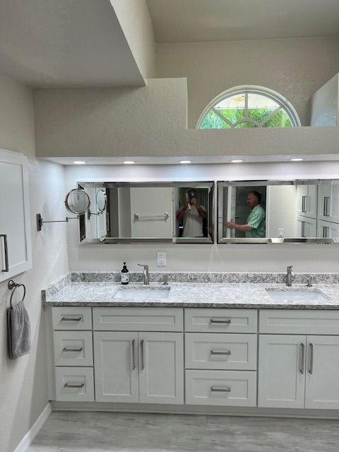 White bathroom with a long vanity, mirrors, and a window above.