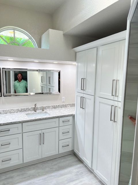 Bathroom with white cabinets, marble countertop, large mirror, and person reflected in the mirror.