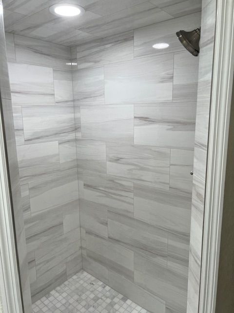 Tiled shower stall with white and gray marble-look tiles. Showerhead, recessed lighting.