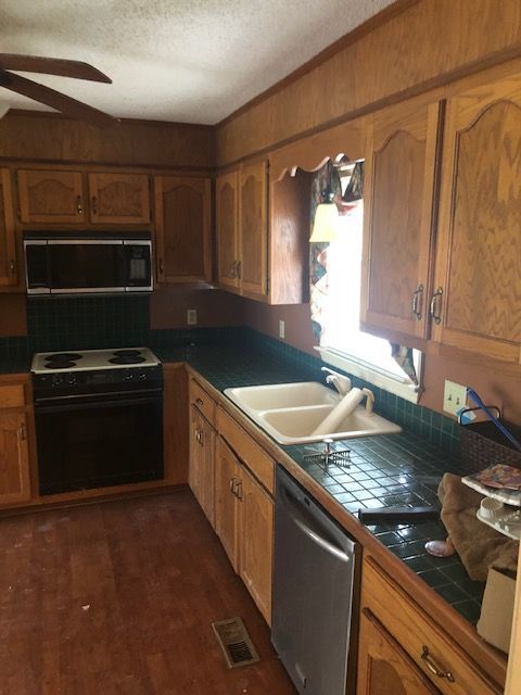 A kitchen with wooden cabinets, black appliances, dark countertops, and a double sink near a window.