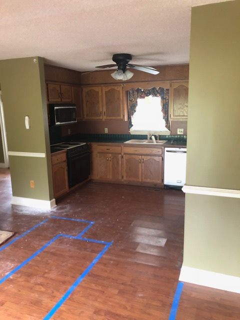 Kitchen with wooden cabinets, black appliances, and green walls. Blue tape on the floor.