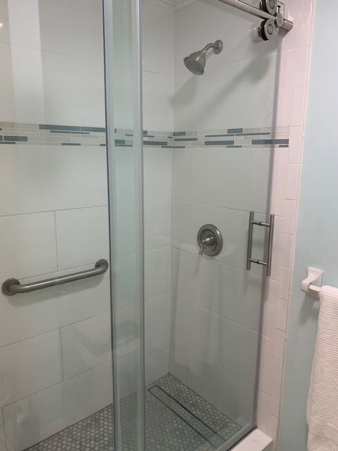 Shower stall with glass door, tile walls, and grab bar.