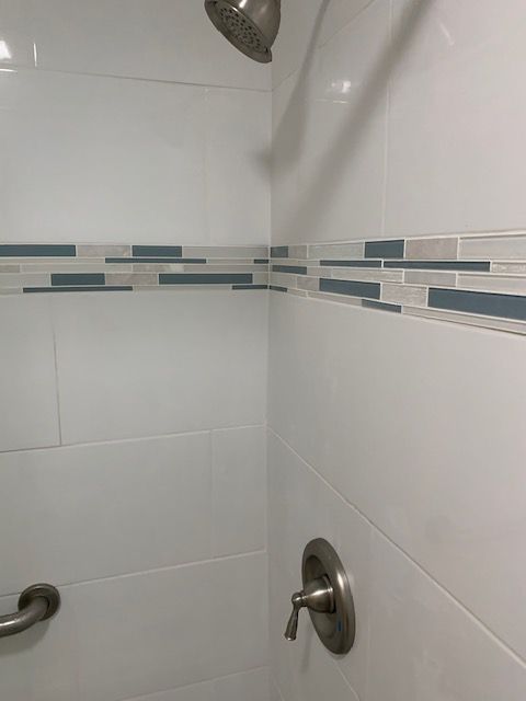 White tiled shower with a decorative blue and gray tile band, chrome fixtures.