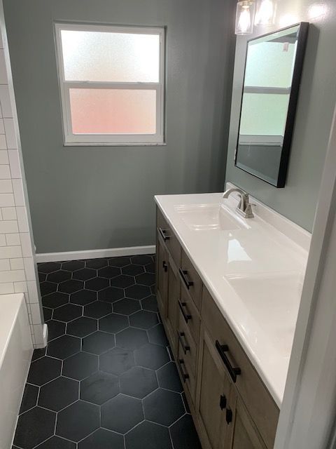 Bathroom with gray walls, black hexagon tile floor, white vanity with double sinks, and a frosted window.