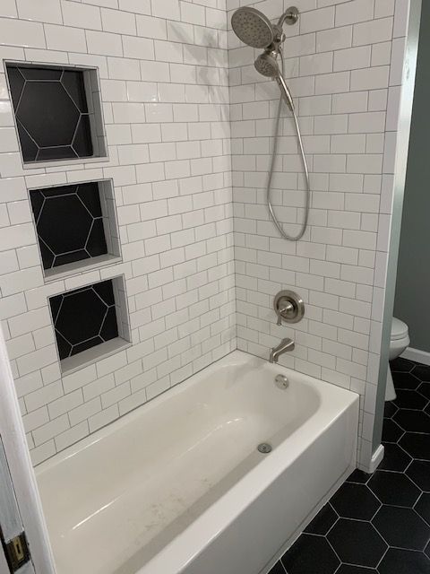 White tiled shower with built-in shelves and a bathtub. Black hexagon tiles line the shelves and floor.