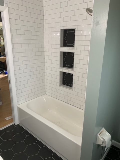 Bathroom with white subway tile, black hexagon floor tile, and three recessed shelves.